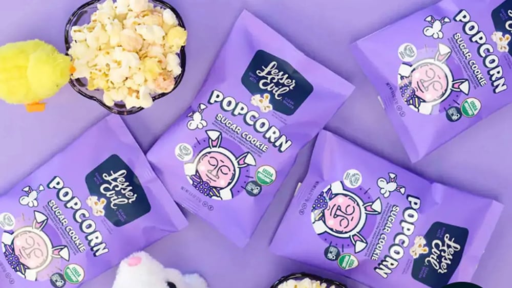 Lesser Evil products sitting on a table next to a bowl of popcorn