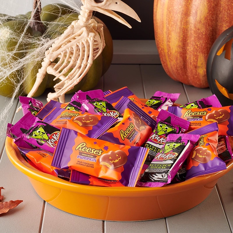 A bowl of assorted Halloween candy beside a carved pumpkin