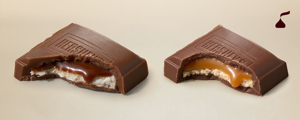Two Hershey’s Creme bars broken open to reveal layers of caramel and cream filling inside a thin milk chocolate shell