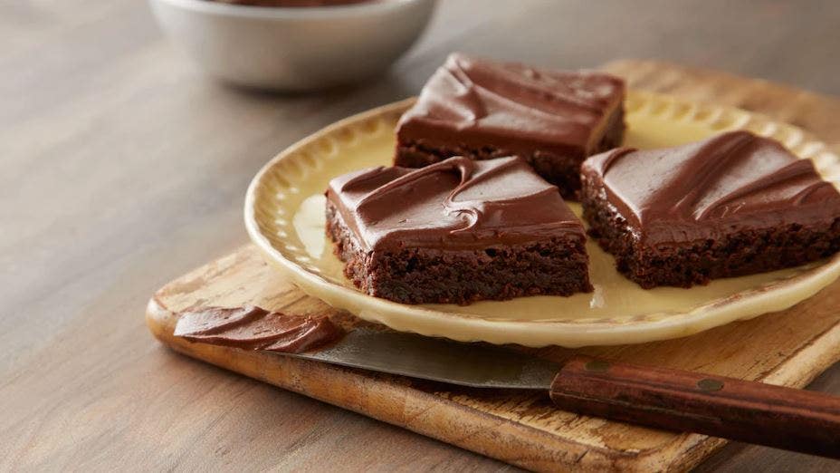 Imagem de 3 pedaços de brownies com cobertura de chocolate HERSHEY’S em um prato bege.