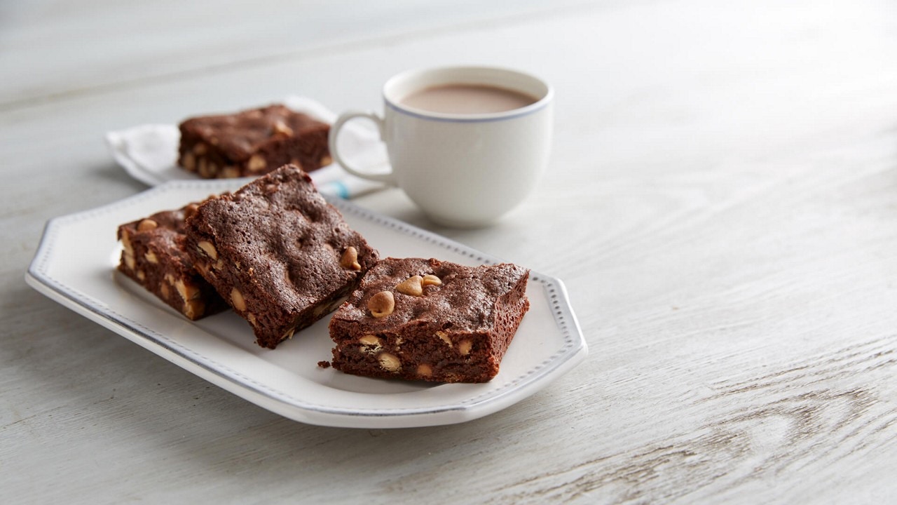 four gluten free brownies on a white plate with a cup of coffee in the background.